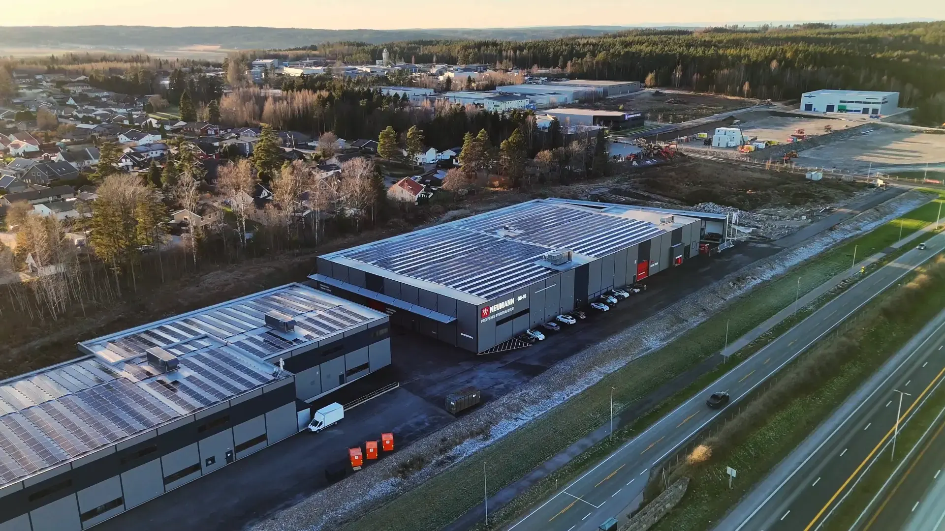 Byggevarehus med stor takflate sett fra luften, med vei og bebyggelse rundt